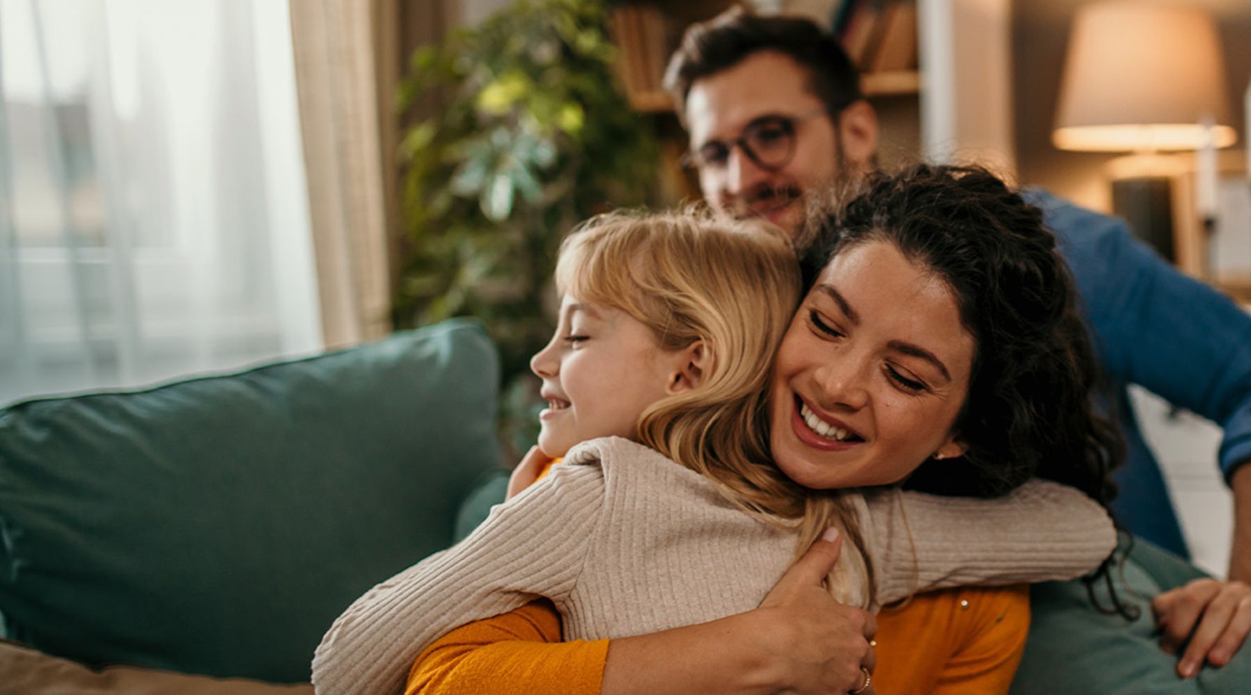 Mutter umarmt ihre Tochter, Vater im Hintergrund
