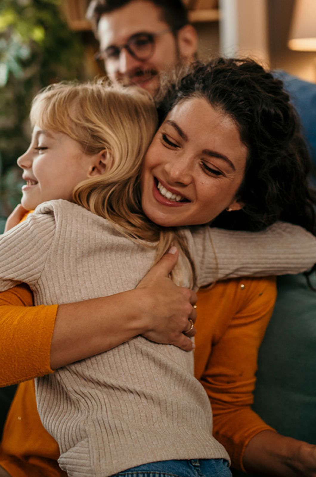 Mutter umarmt ihre Tochter, Vater im Hintergrund